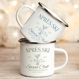 Op de afbeelding: Twee witte emaille mokken op elkaar gestapeld. Elke mok heeft een zilveren rand en een wit handvat. De mokken tonen de tekst "APRÈS SKI", "Social Club" en "KATE'S BACHELORETTE ASPEN, COLORADO" met een martini glas illustratie.