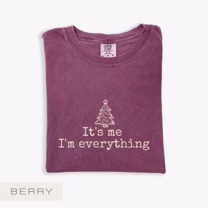 May include: Berry-coloured t-shirt with a crew neck. The shirt features a white Christmas tree graphic and the text "It's me I'm everything". The Comfort Colors brand label is visible at the top. The word "BERRY" is at the bottom.
