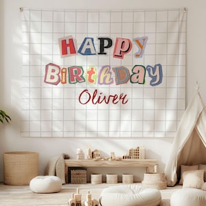 Pode incluir: Uma tapeçaria de parede retangular com um padrão de grade branca sobre um fundo claro. O texto "HAPPY BIRTHDAY" é exibido em um estilo de colagem multicolorido, com o nome "Oliver" impresso em letra cursiva vermelha abaixo.