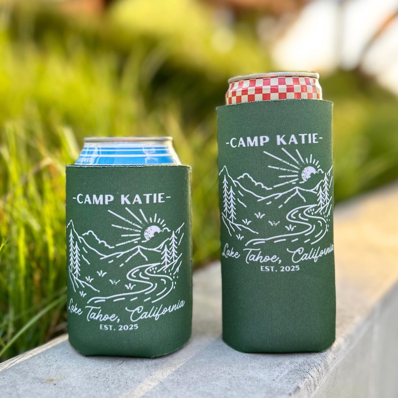 May include: Two green and white insulated can coolers with the text "Camp Katie - Lake Tahoe, California - Est. 2025" printed on them.