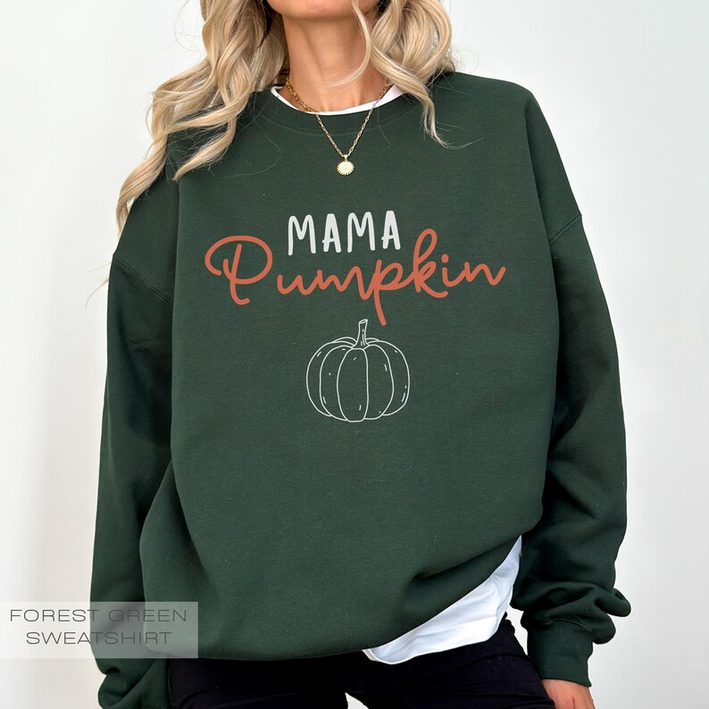Pu&ograve; includere: Felpa verde bosco con il testo "Mama Pumpkin" in lettere bianche e arancioni. Un piccolo grafico di zucca si trova sotto il testo.