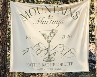 May include: Cream-colored banner with the text "MOUNTAINS & Martinis" and a martini glass illustration. Below the martini glass are mountain illustrations and the text "KATIE'S BACHELORETTE ASPEN, COLORADO".