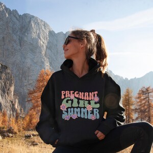 Puede incluir: Sudadera con capucha negra con el texto "Pregnant Girl Summer" en una fuente retro con colores rosa, verde y azul y detalles florales.