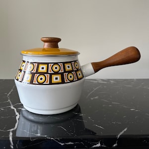 May include: White enamel saucepan with a brown and yellow geometric pattern. The saucepan has a wooden handle and lid.