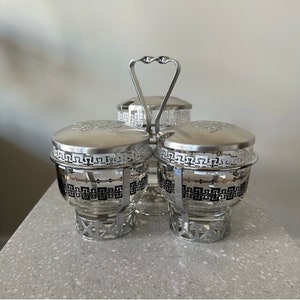 Peut inclure: Un ensemble de trois pots à condiments en argent avec un motif géométrique. L'ensemble comprend trois pots en verre avec des couvercles en argent et un support en argent avec une poignée.