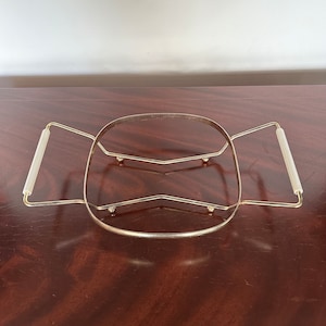 Puede incluir: Una bandeja de servir de metal dorado con dos asas. La bandeja tiene una forma ovalada redondeada y un diseño de alambre.