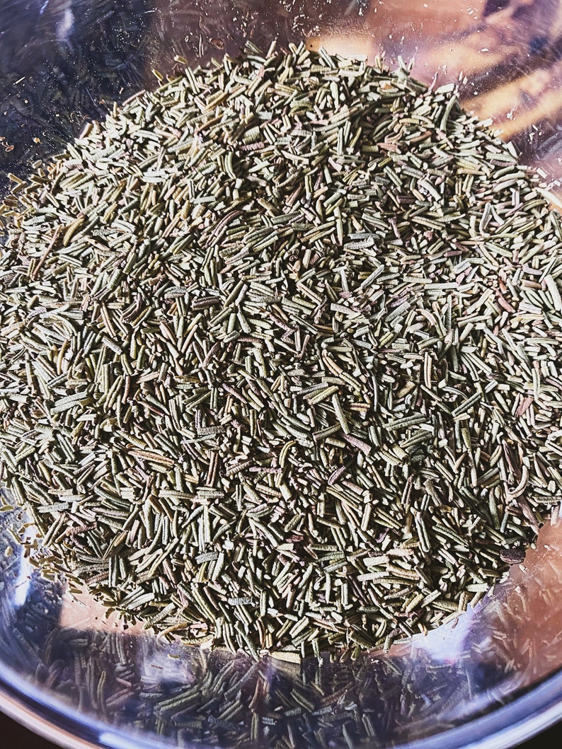 May include: A close-up view of a bowl filled with dried rosemary needles. The needles are a light green color and are arranged in a random pattern.