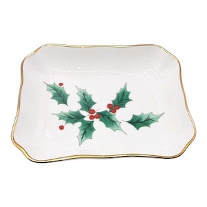 May include: A white rectangular ceramic dish with a gold trim and a holly berry design. The holly leaves are green, and the berries are red. The dish is a festive piece for the holiday season.