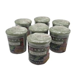 May include: Six sage green votive candles wrapped in clear plastic. Each candle features a label reading Yankee Holiday Sage Samplers Candle with a net weight of 49 grams. The candles are arranged in a cluster, displaying the green wax tops.