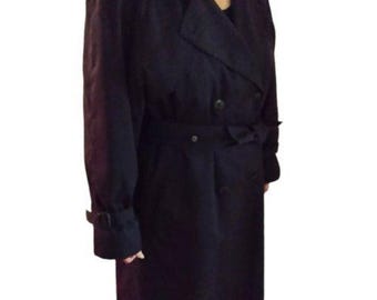 May include: A long, black trench coat with a double-breasted design. The coat features a belt at the waist, button details, and adjustable cuffs. The coat is made of a dark, possibly wool or synthetic material.