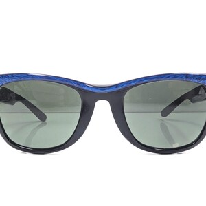 Op de afbeelding: Vintage zonnebril met een zwart montuur en groene glazen. De bovenkant van het montuur heeft een blauw gemarmerd ontwerp. De zonnebril heeft een klassieke cat-eye vorm, op een witte achtergrond.
