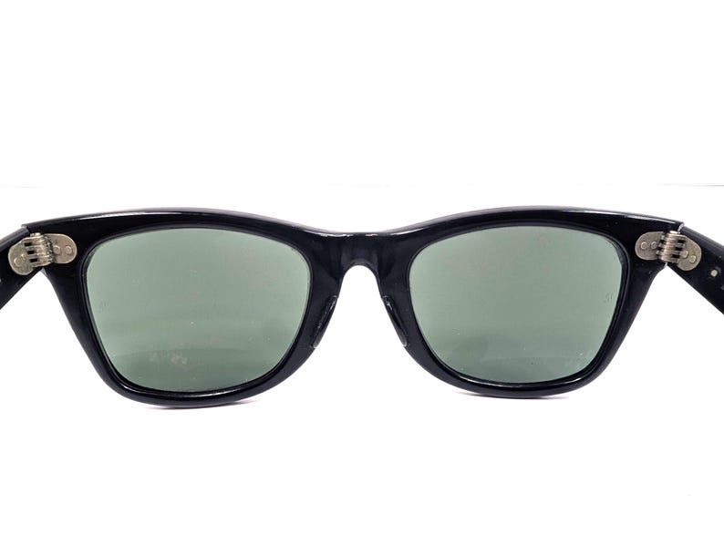 Op de afbeelding: Zwarte zonnebril met een klassiek design. De monturen zijn glanzend zwart en de glazen zijn een gedempt groen. De scharnieren zijn zilverkleurig. Een stijlvol accessoire voor oogbescherming.