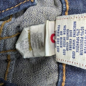 Pode incluir: Vista de perto do interior de uma pe&ccedil;a de roupa de ganga, mostrando costuras e etiquetas de tecido. As etiquetas exibem detalhes da composi&ccedil;&atilde;o do tecido: 88% algod&atilde;o, 10% poli&eacute;ster e 2% spandex. Instru&ccedil;&otilde;es de lavagem vis&iacute;veis.