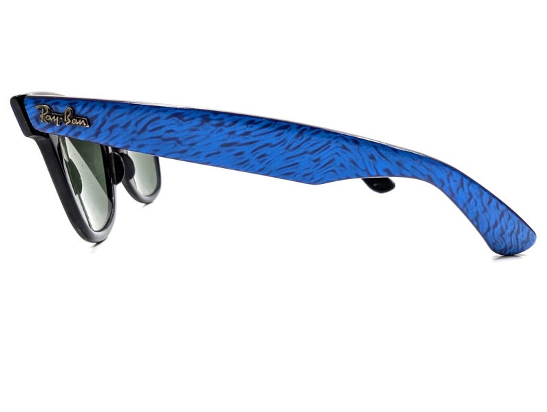 Op de afbeelding: Zonnebril met zwart montuur en blauwgepatroneerde pootjes. Het Ray-Ban-logo is zichtbaar op het montuur. De glazen zijn donkergroen.