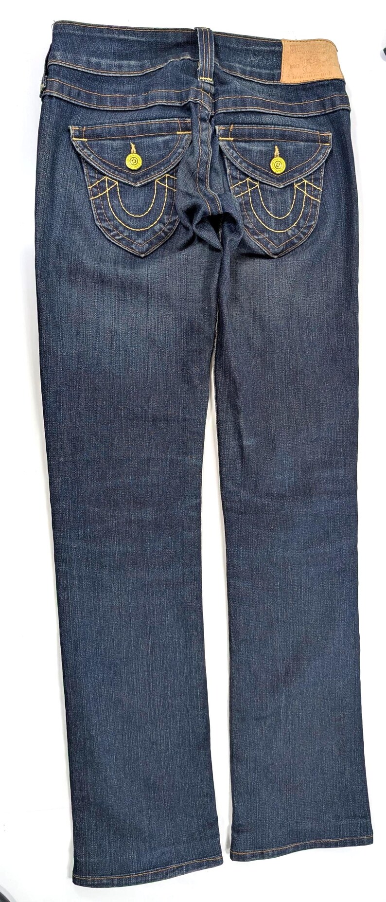 Pode incluir: Jeans de ganga azul escuro com corte reto. Apresentam costuras decorativas douradas nos bolsos traseiros e um remendo de couro na cintura. Os jeans t&ecirc;m um design cl&aacute;ssico de cinco bolsos.