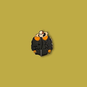 Puede incluir: Pin de esmalte negro con un personaje de dibujos animados que lleva una chaqueta acolchada negra con detalles naranjas y un ribete de piel blanca.