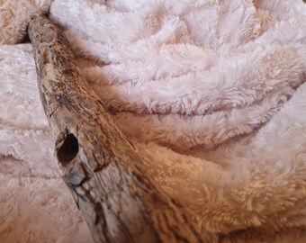 Peut inclure: Une branche de bois brune et usée avec un trou, posée sur une couverture douce et rose en fourrure.