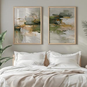 May include: Two framed abstract paintings with a neutral color palette of white, green, and tan. The artwork is displayed above a bed with white bedding and a beige throw blanket. The text "Blue Yellow Gallery" is visible on the bed.