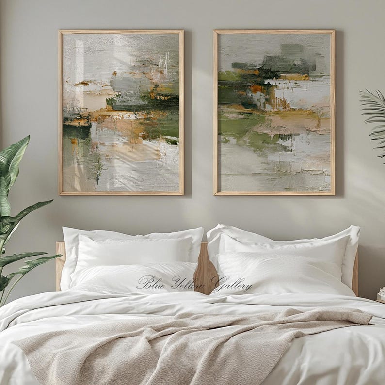 May include: Two framed abstract paintings with a neutral color palette of white, green, and tan. The artwork is displayed above a bed with white bedding and a beige throw blanket. The text "Blue Yellow Gallery" is visible on the bed.