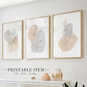 Puede incluir: Tres impresiones minimalistas de arte lineal con formas abstractas en tonos melocotón y gris. Las impresiones presentan dibujos lineales simples de flores y hojas. Las impresiones están enmarcadas en marcos de madera natural y están colgadas en una pared blanca.