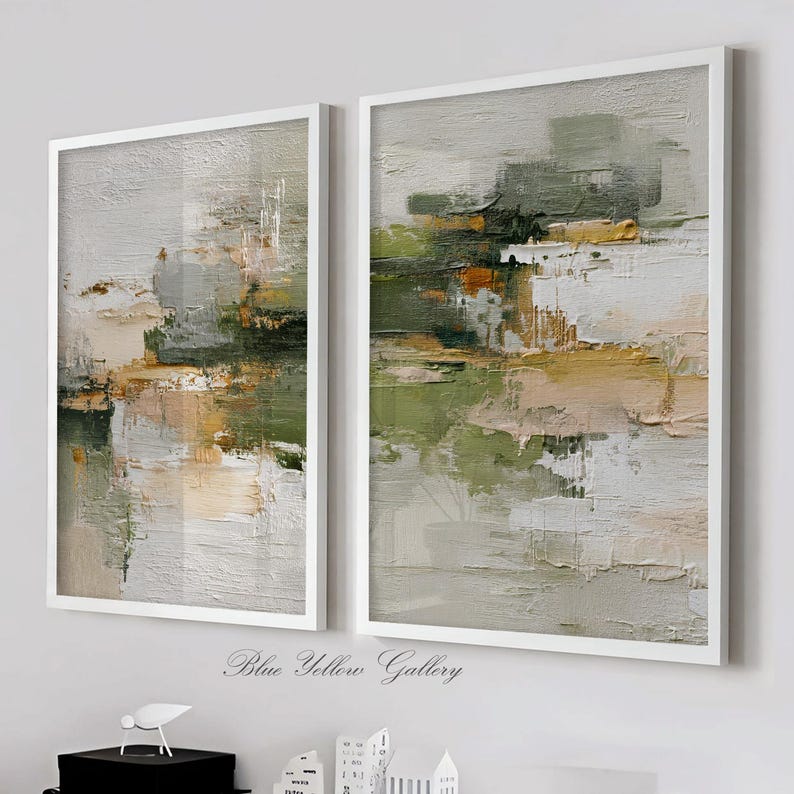 May include: Two framed abstract paintings with white borders. The artwork features textured brushstrokes in shades of green, beige, gray, and yellow. The paintings are displayed on a white wall. The text "Blue Yellow Gallery" is at the bottom.