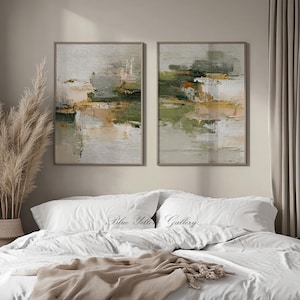 May include: Two framed abstract paintings with neutral tones of green, beige, and white. The artwork features textured brushstrokes and a landscape-like composition. The paintings are displayed above a bed with white linens.