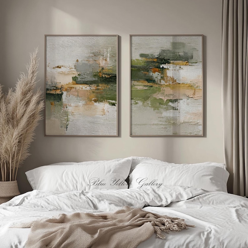 May include: Two framed abstract paintings with neutral tones of green, beige, and white. The artwork features textured brushstrokes and a landscape-like composition. The paintings are displayed above a bed with white linens.