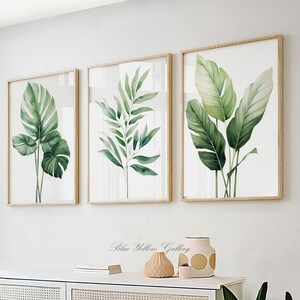 May include: Three framed botanical prints featuring watercolor illustrations of green leaves. The prints are in light wood frames and hang on a white wall. The artwork includes a variety of leaf shapes and sizes, creating a natural and calming aesthetic.