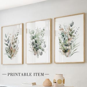 Pode incluir: Três impressões botânicas emolduradas com ilustrações em aquarela de folhagens verdes e marrons. As impressões estão em molduras de madeira clara e são exibidas em uma parede branca. O texto "PRINTABLE ITEM" está na parte inferior.