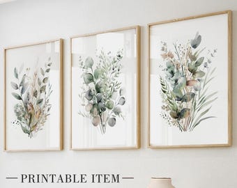 Puede incluir: Tres impresiones botánicas enmarcadas con ilustraciones de acuarela de follaje verde y marrón. Las impresiones están en marcos de madera clara y se exhiben en una pared blanca. El texto "PRINTABLE ITEM" está en la parte inferior.
