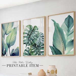 Puede incluir: Tres impresiones enmarcadas de hojas tropicales verdes. Las impresiones están en marcos de madera y están colgadas en una pared blanca. El texto "Blue Yellow Gallery - PRINTABLE ITEM -" está debajo de las impresiones.