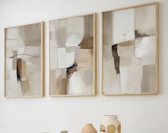 May include: Three abstract paintings in beige, brown, and white tones, framed in natural wood, hanging on a white wall. The paintings are arranged in a row, with the middle painting slightly higher than the other two.