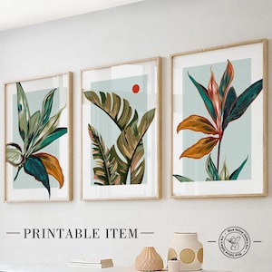 Op de afbeelding: Drie ingelijste prints met een tropisch thema. Elke print toont een andere gestileerde illustratie van tropische bladeren in tinten groen, oranje en blauw tegen een lichtblauwe achtergrond.