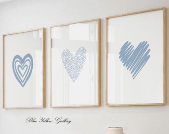 Könnte beinhalten: Drei gerahmte Drucke mit blauen Herzmotiven. Die Herzen sind in verschiedenen Stilen gehalten, eines ist mit kleinen Punkten gefüllt, eines ist ein geschichtetes Herz und das dritte ist ein gekritztes Herz. Die Rahmen sind aus hellem Holz.