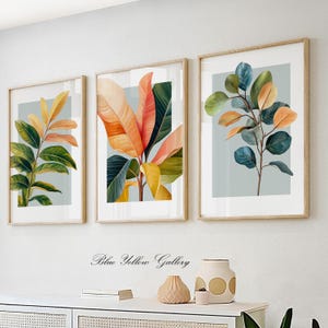 May include: Three framed botanical prints with a light blue background. The prints feature stylized illustrations of green, yellow, orange, and red leaves.