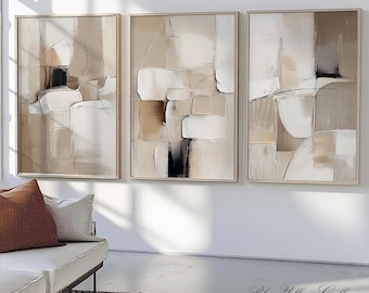 May include: A set of three abstract paintings in shades of beige, brown, and white. The paintings are framed in a light wood frame and are hung on a white wall.