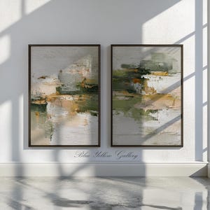 May include: Two framed abstract paintings with a textured, layered appearance. The artwork features a palette of muted greens, beige, and gold, with dark brown frames. The paintings are displayed on a white wall, with the text "Blue Yellow Gallery" at the bottom.