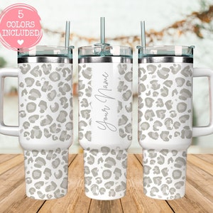 Peut inclure: Gobelet blanc avec un motif léopard gris, une poignée et un couvercle transparent. Le gobelet comprend une paille argentée et le texte "Your Name" en cursive. Un cercle rose avec le texte "5 COLORS INCLUDED" est en haut à gauche.
