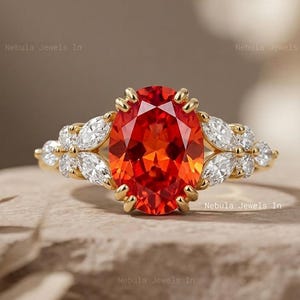 May include: A gold ring featuring a large oval-cut vibrant orange gemstone at the center, flanked by a cluster of marquise and round-cut clear white stones on each side, set in a polished yellow gold band with a prong setting design.