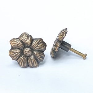 May include: Two antique gold-toned flower-shaped cabinet knobs with a screw attachment.