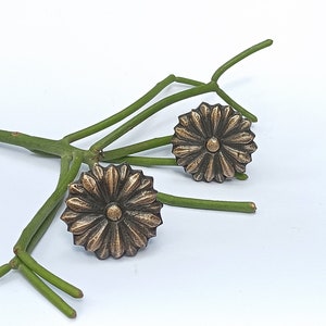 Peut inclure: Deux boutons de cabinet en laiton antique avec un motif floral. Les boutons ont un centre surélevé et un motif texturé en forme de soleil.
