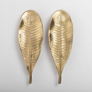 May include: Two gold leaf-shaped decorative wall sculptures. The leaves have a detailed vein pattern and a smooth, metallic finish.