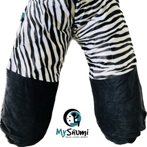 Pode incluir: Um travesseiro de gravidez com estampa de zebra em preto e branco com acabamento preto e turquesa. O travesseiro tem formato de U e tem um fundo de veludo preto. O travesseiro tem o texto "My Snümi Relax - Sleep - Repeat" na parte inferior.