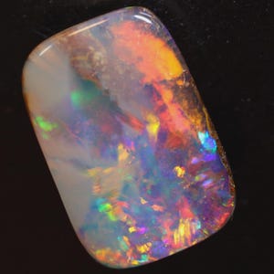 Peut inclure: Une pierre d'opale polie de forme rectangulaire. La pierre présente un jeu de couleurs vibrant, notamment des teintes de rouge, d'orange, de jaune, de bleu et de vert. L'opale a une base blanc laiteux avec des reflets irisés.