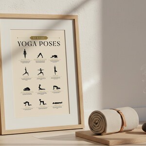 May include: A framed print displaying 12 basic yoga poses in black on a cream background. The print is in a light wood frame. A rolled-up beige yoga mat with a leather strap, and a small black candle holder sit on a wooden tray.