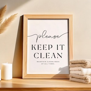 Può includere: Una stampa incorniciata con le parole "Please Keep It Clean" in scrittura nera. La cornice è in legno chiaro e la stampa è esposta con asciugamani piegati e candele.