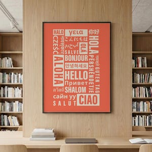 May include: A rectangular wall art print featuring a coral-red background with the word "HELLO" and various international greetings in white text, including "ALOHA," "BONJOUR," "CIAO," and "SALVE," all enclosed in a thin black frame.