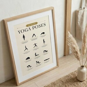 May include: A framed print featuring 12 basic yoga poses in black silhouettes on a cream background. The print is in a light wood frame and leans against a wall. The text "12 Basic Yoga Poses" is at the top.