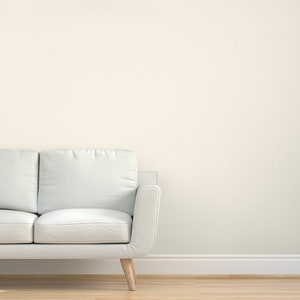 May include: A white sofa with a light wood frame sits in front of a white wall with white baseboards. The sofa has two cushions and a single armrest.