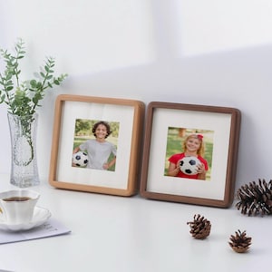 May include: Two wooden picture frames with a light brown and dark brown finish. Each frame holds a photo of a child holding a football. The photo on the left shows a boy wearing a blue shirt and the photo on the right shows a girl wearing a red shirt.